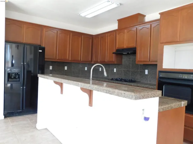 Kitchen with black appliances, backsplash, an island with sink, wood finish cabinets, and a kitchen bar