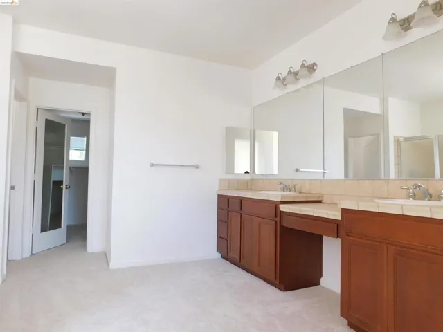 Bathroom with double vanity, light colored carpet, and a shower stall