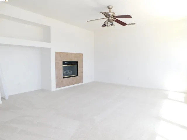 Unfurnished living room with light carpet, a ceiling fan, and a tile fireplace