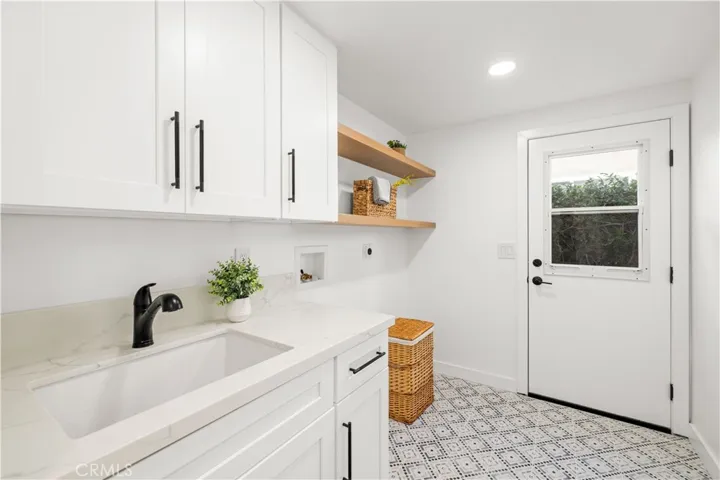 This laundry room features clean cabinetry, a functional sink, and open shelving, with direct access to the exterior for added convenience.