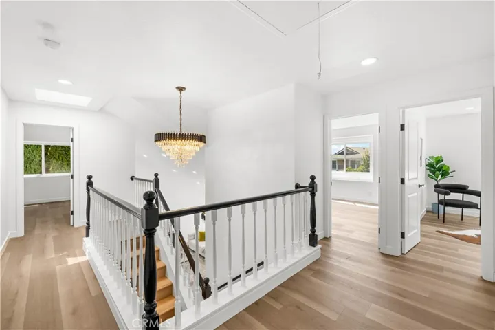 Open upstairs landing with elegant railing, chandelier lighting, and access to surrounding bedrooms filled with natural light.