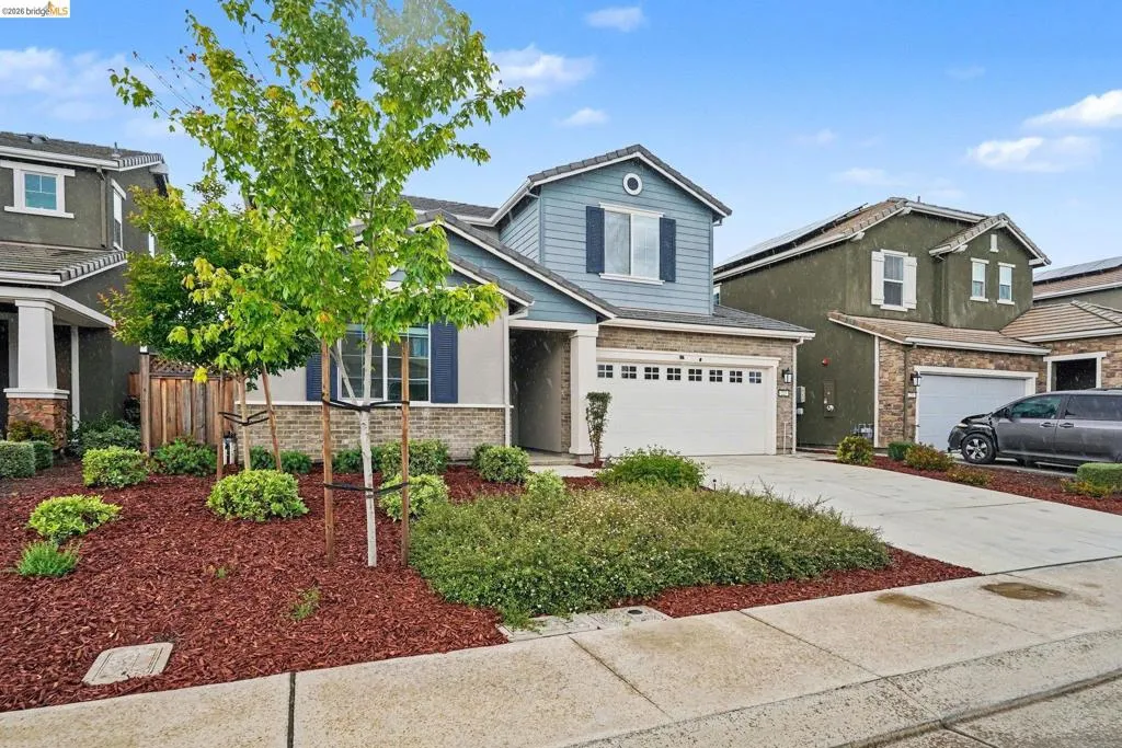 Contemporary two-story residence featuring a two-car garage, stone and siding exterior, and a manicured front yard with mature trees