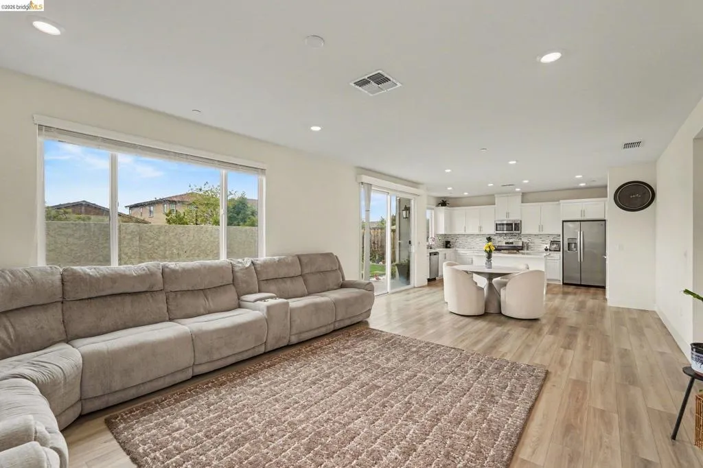 Open-concept living space featuring wood-finish flooring, recessed lighting, a kitchen with white cabinetry, and sliding glass doors leading to the exterior