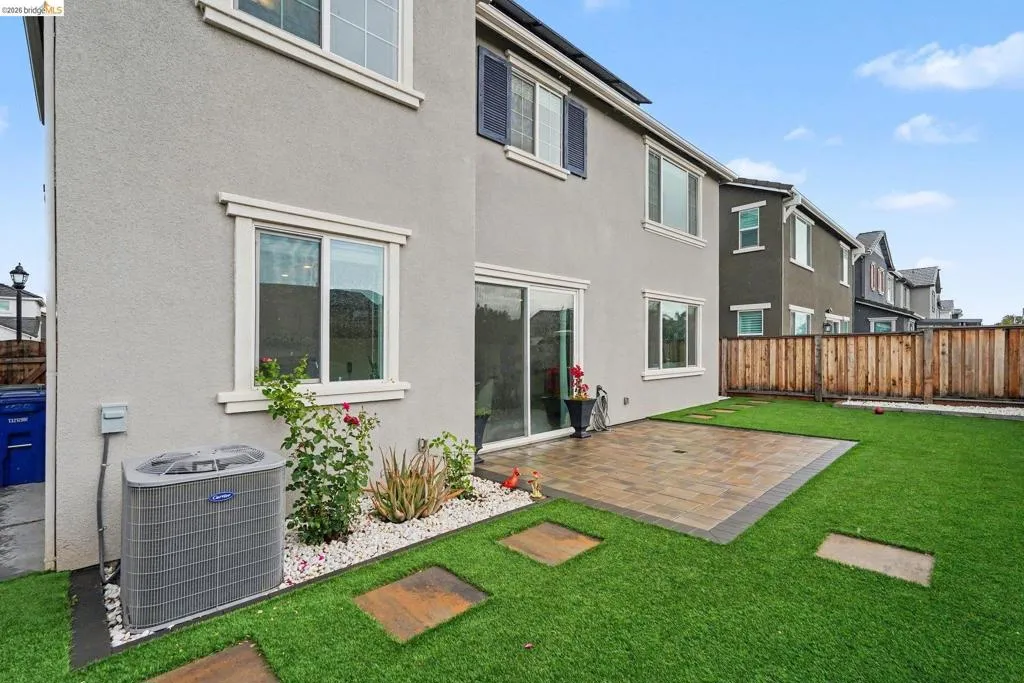 Backyard featuring a paver patio area, artificial turf lawn, and stepping stones