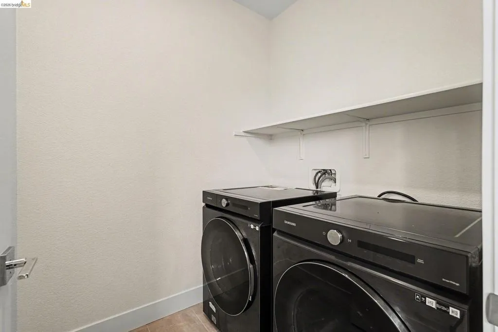 Dedicated laundry space featuring a white wall shelf, textured walls, and a light-colored baseboard