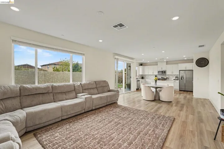 Open-concept living space featuring wood-finish flooring, recessed lighting, a kitchen with white cabinetry, and sliding glass doors leading to the exterior