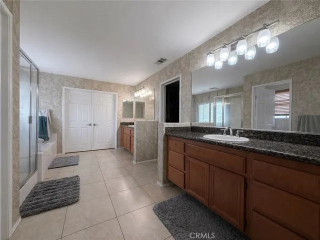 Primary ensuite bathroom with double sinks, jetted soaker tub, walk-in shower, walk-in closet, and toilet with a door. Double doors at end go to nursery/office/weight room.