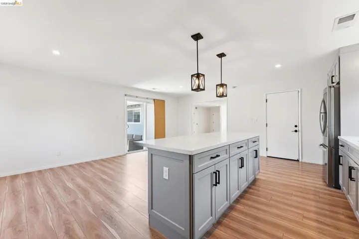Two tone kitchen with a center island, light wood-style floors, two tone cabinetry, freestanding refrigerator, and pendant lighting