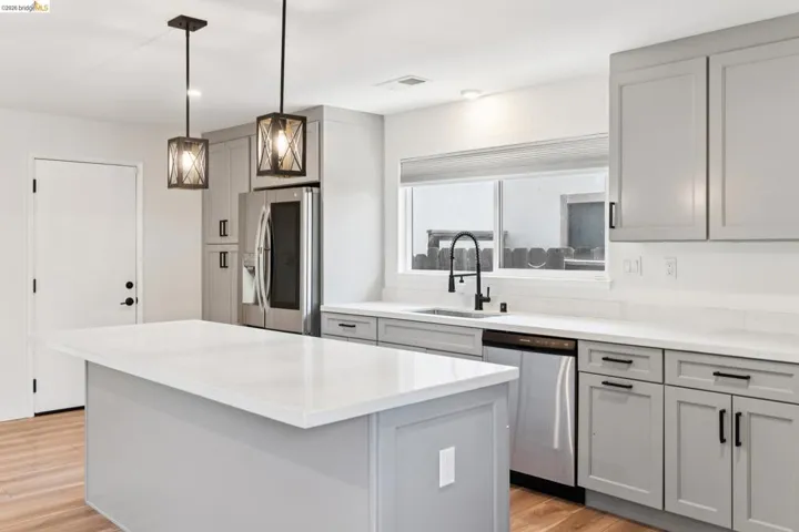 Kitchen with gray cabinetry, stainless steel appliances, light wood finished floors, decorative light fixtures, and a kitchen island