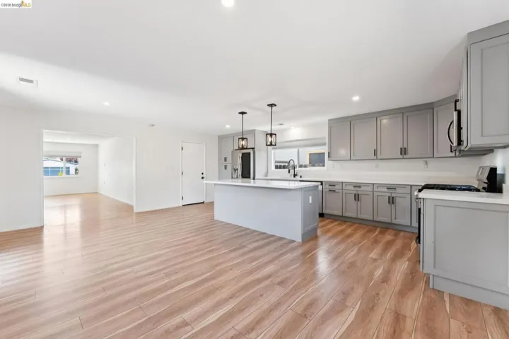 Kitchen featuring gray cabinetry, a center island, light wood-style flooring, stainless steel appliances, and decorative light fixtures