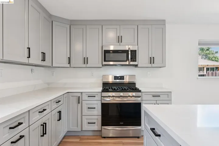 Kitchen featuring stainless steel appliances, light wood-style flooring, light stone counters, and gray cabinetry