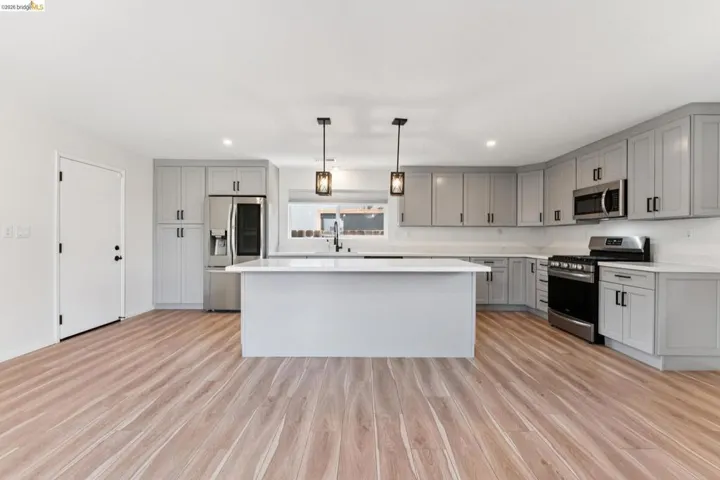 Kitchen with gray cabinetry, stainless steel appliances, a center island, light wood-type flooring, and pendant lighting