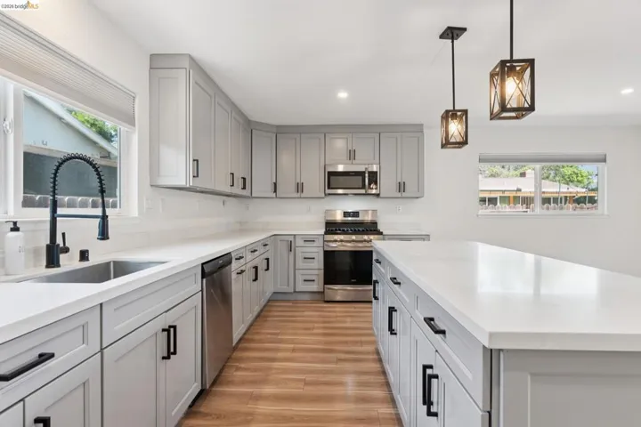 Kitchen with stainless steel appliances, gray cabinetry, decorative light fixtures, light wood finished floors, and a kitchen island