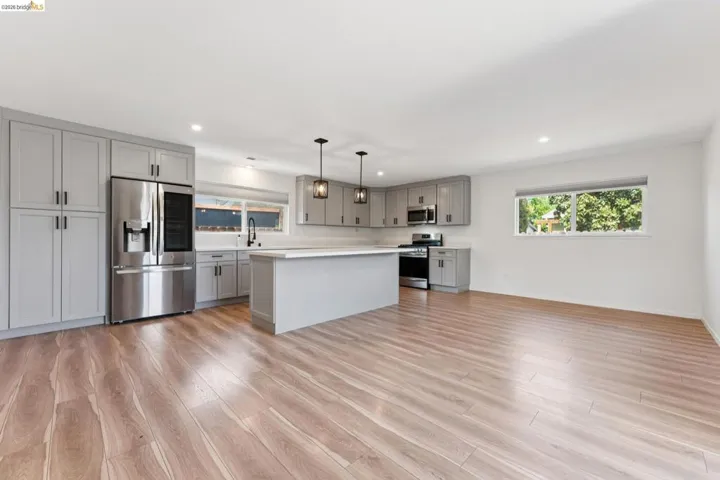Kitchen with gray cabinetry, light countertops, stainless steel appliances, pendant lighting, and a kitchen island