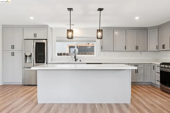 Kitchen with stainless steel appliances, a kitchen island, hanging light fixtures, and light wood-style flooring