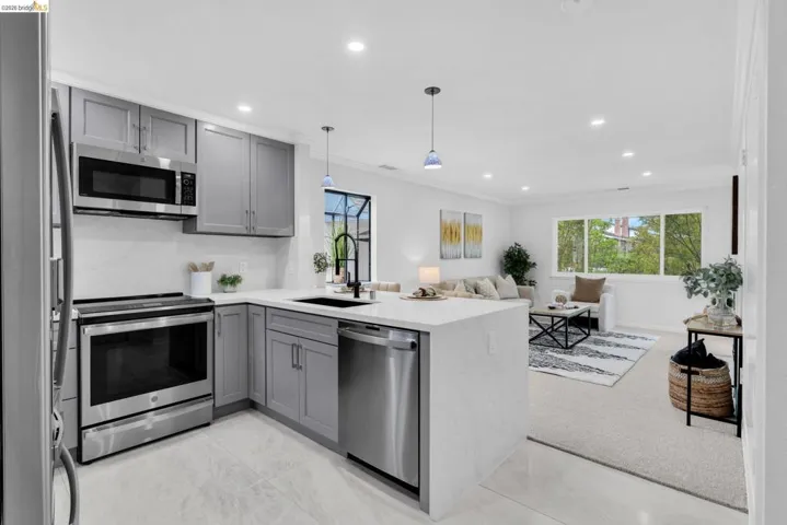 Kitchen with gray cabinets, a peninsula, stainless steel appliances, light stone countertops, and open floor plan