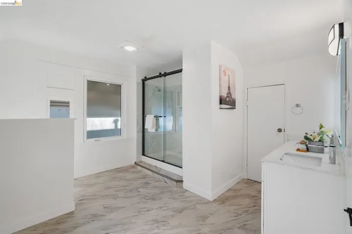 Spacious bathroom featuring marble-look tile flooring, a glass-enclosed shower with a black frame, and a white vanity with an integrated sink