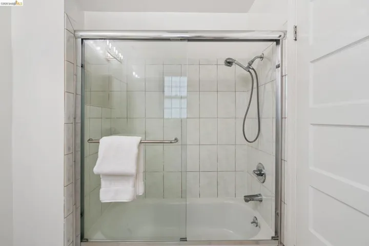 Bathtub with a glass sliding shower door featuring a chrome handle, chrome shower head, and chrome fixtures