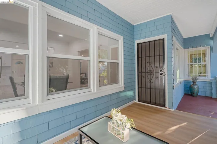 Inviting front porch featuring blue shingle siding, white trim windows, a decorative security screen door, wood-finish flooring, and a white beadboard ceiling