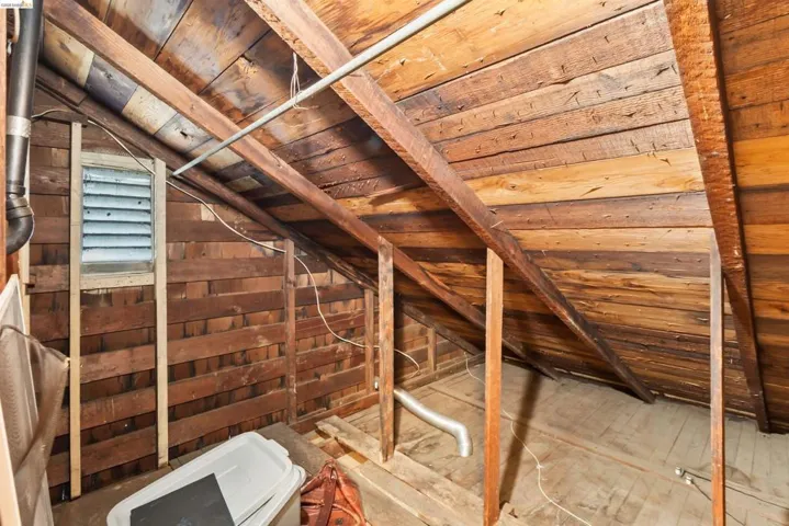 Unfinished attic space featuring exposed wood beams and plank walls