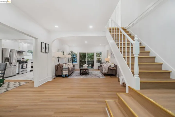 Inviting interior featuring wood-finish flooring, a prominent staircase with white balusters, recessed lighting, and a white color palette