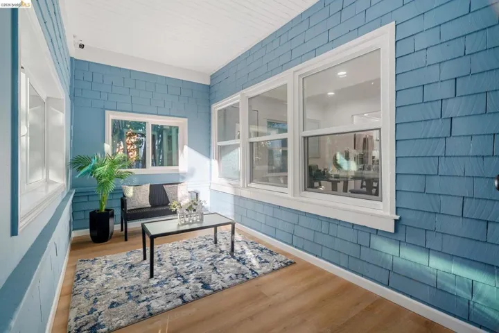 Enclosed porch featuring blue shingle siding, wood-finish flooring, white window trim, multiple windows, and a white beadboard ceiling