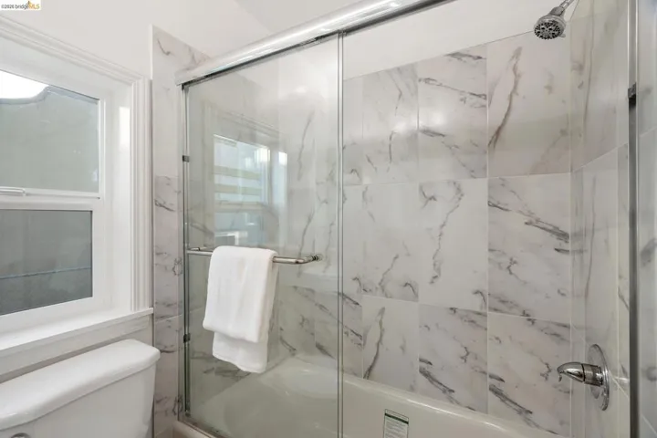 Bathtub and shower combination featuring large format marble-look tile surround, glass shower enclosure, and a chrome shower head with matching fixtures