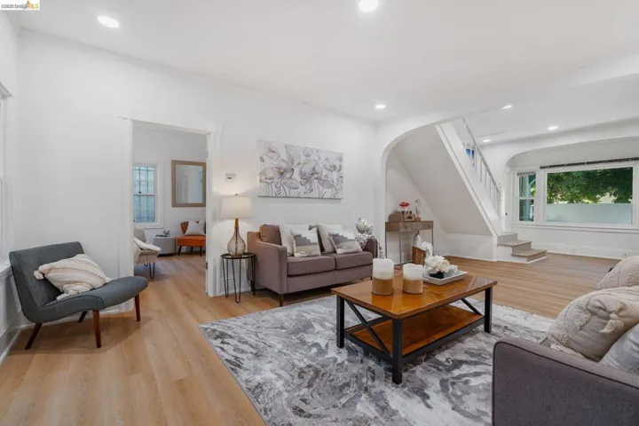 Bright living area featuring recessed lighting, wood-finish flooring, a prominent staircase, and an arched entry
