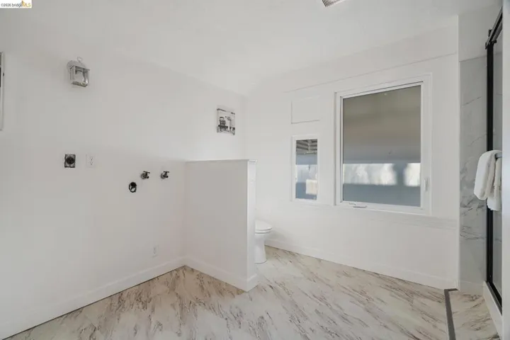 Bathroom featuring marble-look floor tile, white walls, and a shower enclosure with a dark frame