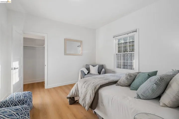Bedroom featuring light wood-finish flooring, white walls, and a window with security bars