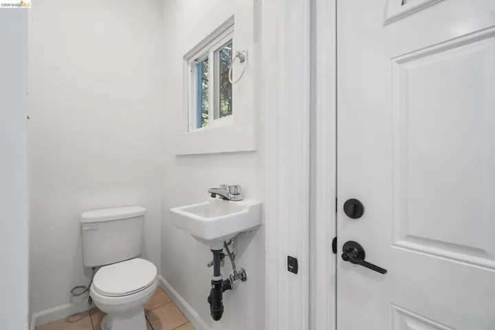 Compact powder room featuring a wall-mounted sink with a chrome faucet, a standard toilet, and a window for natural light
