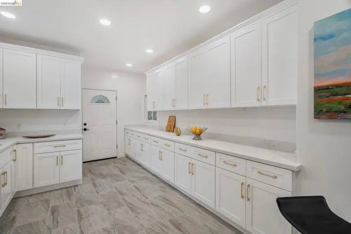 Modern kitchen featuring extensive white shaker cabinetry with gold-tone hardware, white countertops, and a white subway tile backsplash