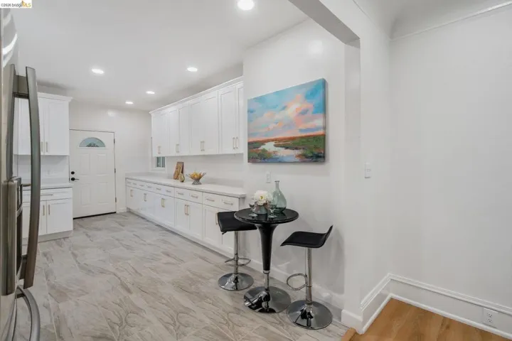 Contemporary kitchen featuring extensive white cabinetry with gold-finish hardware, light-toned countertops, recessed lighting, and a white paneled door with an arched glass insert