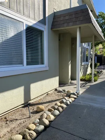 Stucco exterior featuring white-framed windows, a covered entryway with supporting columns, and a landscaped rock border