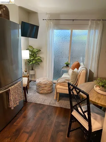 Living area featuring wood-finish flooring, a wall-mounted television, and a window with patterned privacy film and sheer drapes