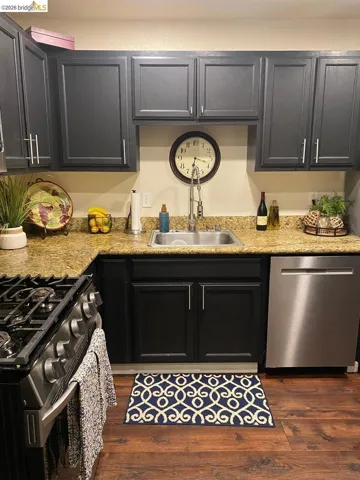 Kitchen featuring dark cabinetry with brushed nickel hardware, a stainless steel sink with a pull-down faucet, a gas range, a stainless steel dishwasher, and wood-finish flooring