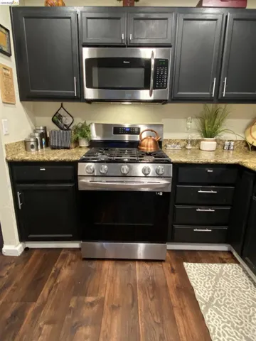 Kitchen featuring dark cabinetry, stainless steel appliances, speckled countertops, and wood-finish flooring