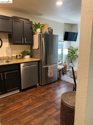 Kitchen area featuring dark cabinetry, stainless steel appliances, wood-finish flooring, and a light-toned countertop