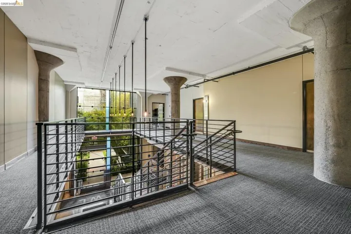 Open-concept interior featuring a multi-level atrium with glass walls, concrete structural columns, exposed ceiling joists, and contemporary pendant lighting