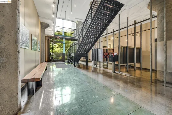 Industrial-style entryway featuring a metal staircase with perforated treads, polished concrete flooring, exposed concrete columns, a built-in wooden bench, and floor-to-ceiling windows