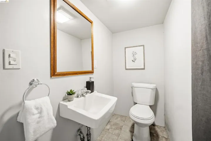 Compact powder room featuring a wall-mounted sink, a toilet, a framed mirror, and light-toned flooring