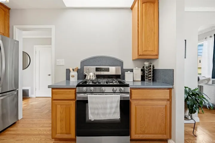 Stainless steel gas range with a matching backsplash, flanked by wood cabinetry, set against light gray walls with wood-finish flooring