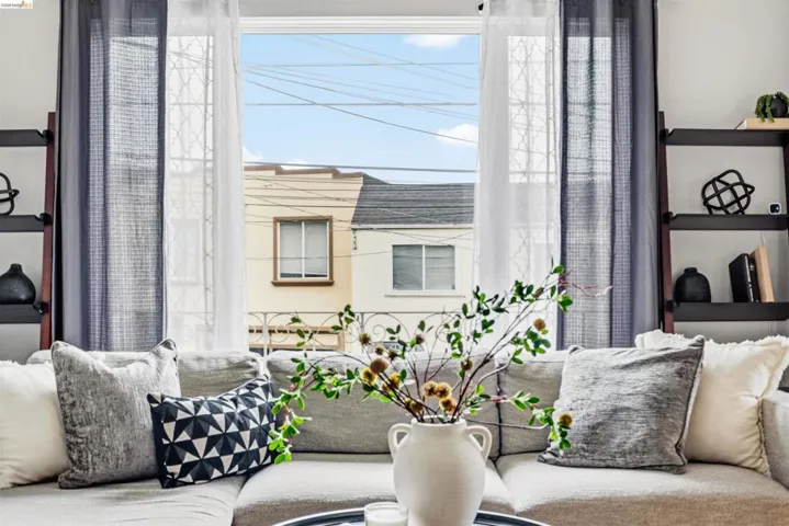 Bright window with white and sheer curtain panels, flanked by two multi-tiered shelving units