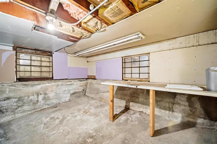 Basement space featuring exposed concrete walls and flooring, two gridded windows, and an exposed ceiling with visible joists and insulation