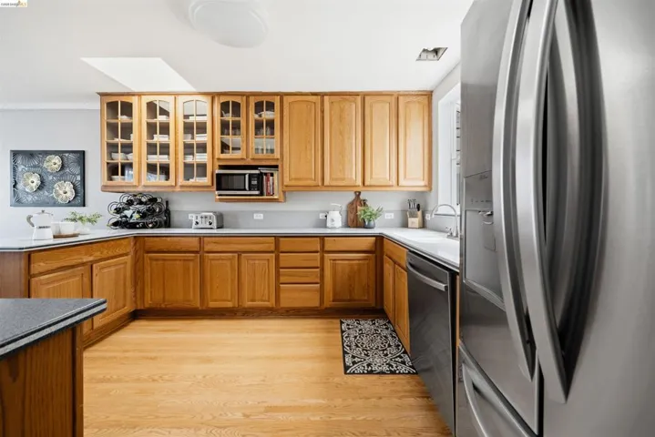 Kitchen featuring wood-finish cabinetry, light countertops, wood-finish flooring, a built-in microwave, and stainless steel appliances