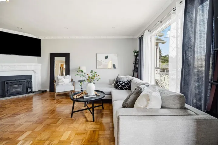 Living area featuring parquet wood flooring, a decorative fireplace with a white mantel, and a large window with direct outdoor access