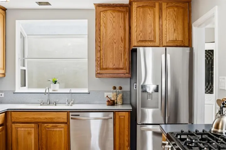 Kitchen featuring wood cabinetry, stainless steel appliances, a corner sink with a gooseneck faucet, light gray countertops, and a gas range