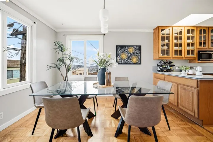 Dining area featuring wood-finish flooring, two large windows, a built-in microwave, and wood cabinetry with glass-front uppers and under-cabinet lighting