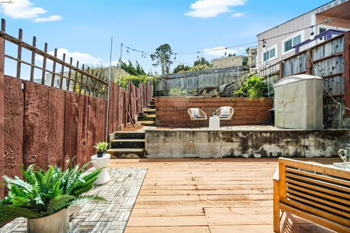 Tiered outdoor area featuring a spacious wood-finish deck, concrete retaining walls, and string lighting