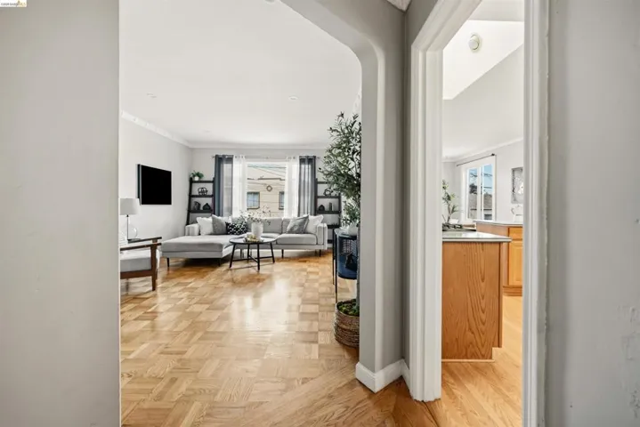 Parquet wood-finish flooring extends through the living space, featuring crown molding and a large window with natural light